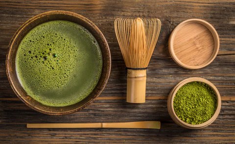 Ceremonial matcha powder with a matcha whisk, spoon and a cup of matcha to drink.
